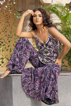Woman wearing a purple and black patterned outfit sitting outdoors.