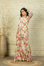 A woman modeling the Anam Ivory Sharara Set, featuring a floral pattern with sequin, cut dana, and mirror embellishments, consisting of a short kurta and flowy sharara pants.