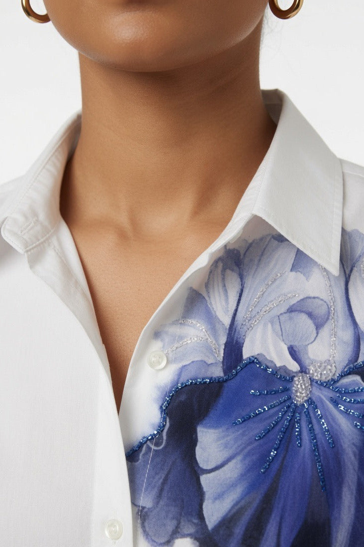 Close-up of a model wearing a white button-up shirt with a large blue and lavender floral applique on the chest.