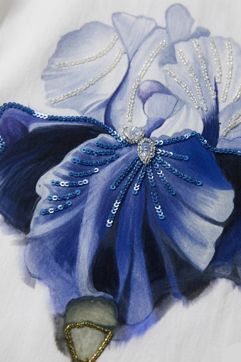 A close-up of a blue and lavender floral artwork with sequined detailing on a white background.