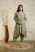 A woman standing in a traditional pose wearing a green tunic and dhoti set with floral and sequin detailing.