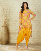 A woman wearing a yellow high-low tunic set with sequin, pearl, and mirror embellishments, paired with dhoti pants.
