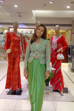 A woman wearing a light green embroidered kurta and matching green pants stands in a clothing store between two mannequins dressed in red traditional outfits.
