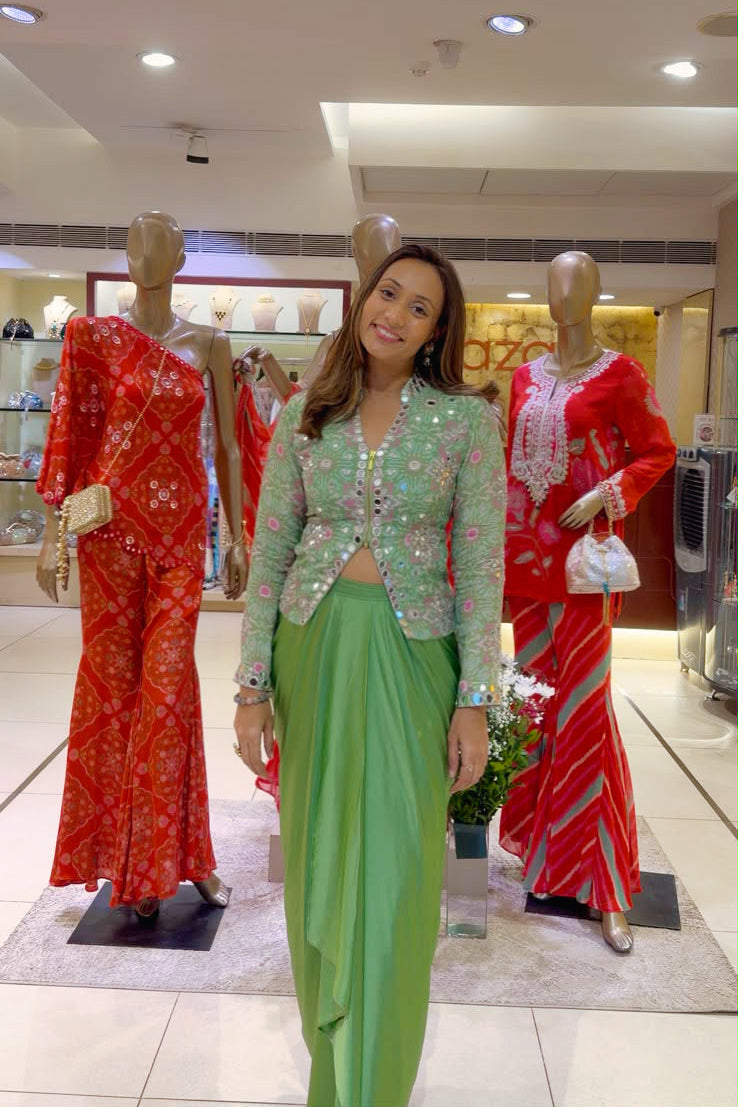 A woman wearing a light green embroidered kurta and matching green pants stands in a clothing store between two mannequins dressed in red traditional outfits.