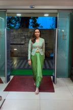 A woman wearing a light green embroidered kurta with a matching green skirt walks through open glass doors in a building lobby.