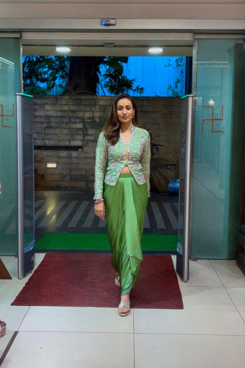 A woman wearing a light green embroidered kurta with a matching green skirt walks through open glass doors in a building lobby.