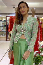 A woman modeling a light green embroidered jacket with pink floral details and a matching green skirt in a clothing store.
