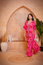 Woman in a pink patterned dress standing in a room with decorative arch and plants.