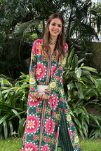 A woman standing outdoors wearing a green and pink floral long kurta set with front open design and paired with pants.