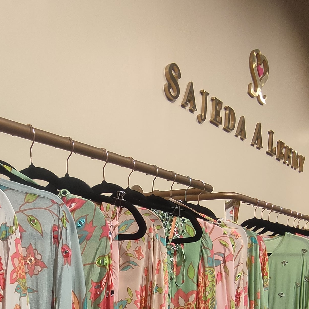 Display of colorful floral dresses on hangers with 'Sajeda Al Rehman' branding.